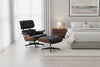 A black full grain leather Herman Miller  Eames lounge chair with a walnut wood structure and a matching ottoman, set against a white background.